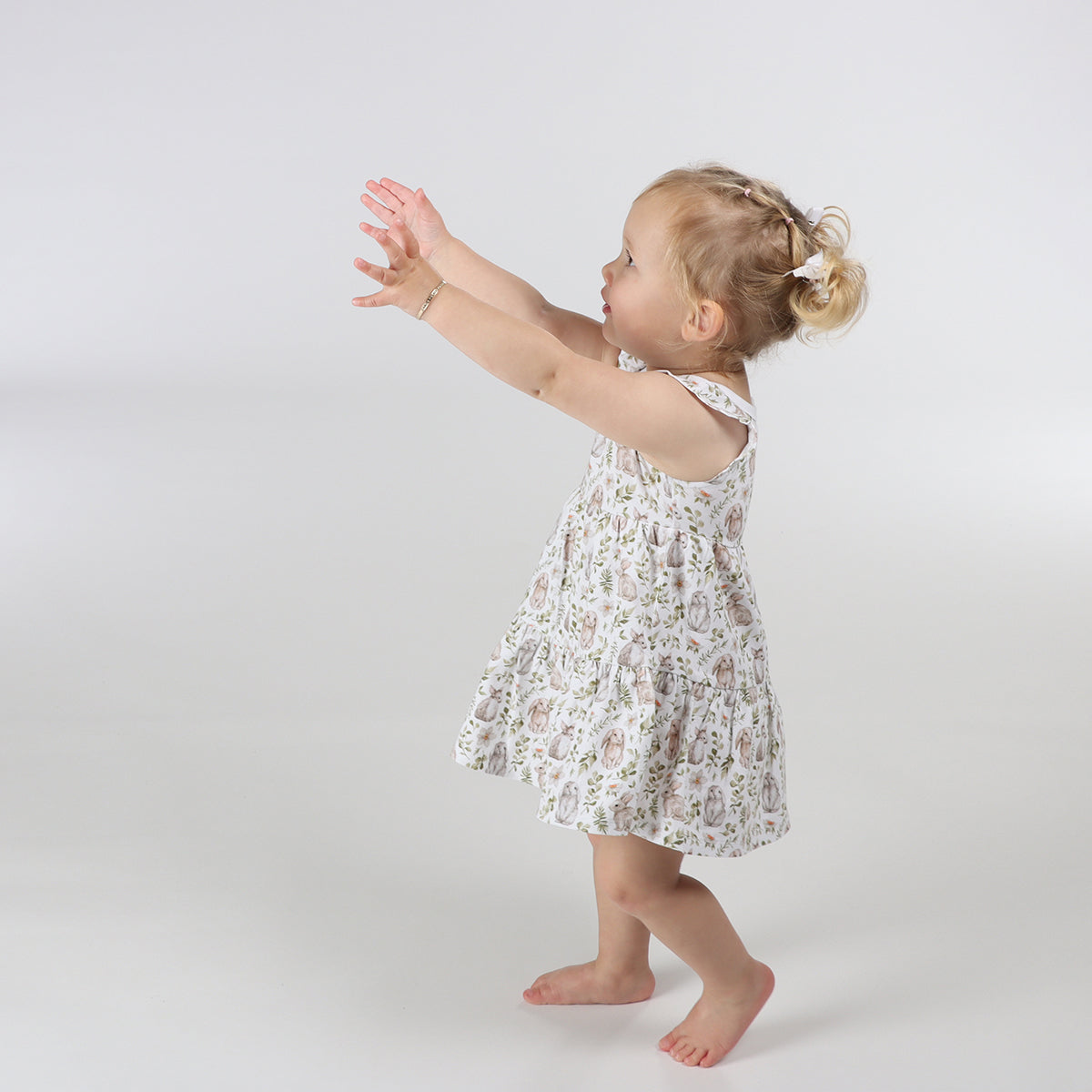Little girl reaching out for something while wearing Little bee cotton tiered dress in white with bunny print 