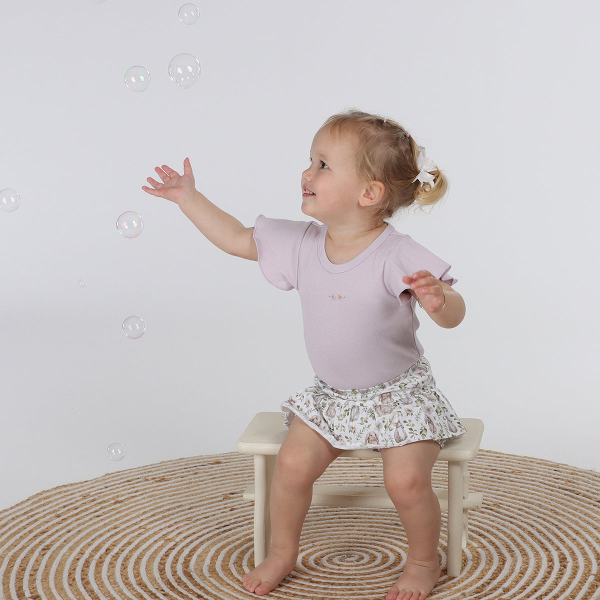 little girl sitting a stool and trying to get bubbles while wearing Little Bee By Dimples Bunny Cotton Skort 