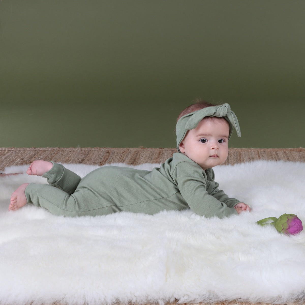 Baby playing, wearing Arctic Adventure Merino Zip Baby grow and headband in Moss from dimples in New Zealand