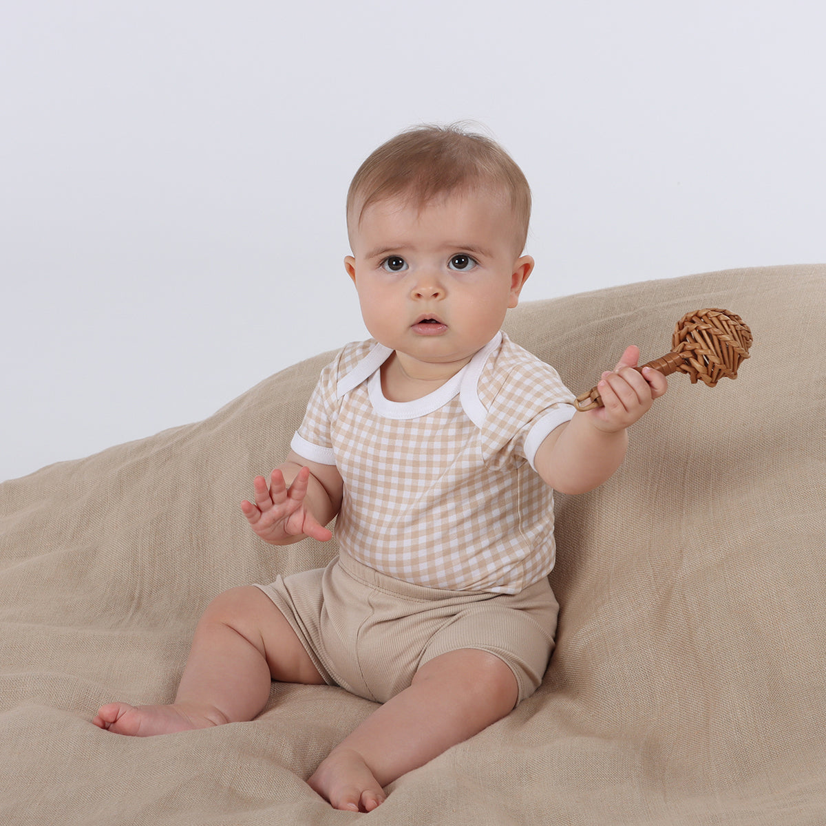 Baby wearing Organic cotton gingham bodysuit and cotton sand shorts playing with rattle