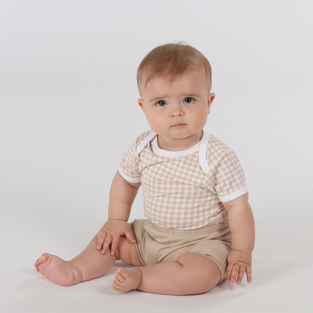 Baby wearing Organic cotton gingham bodysuit and cotton sand shorts playing with rattle