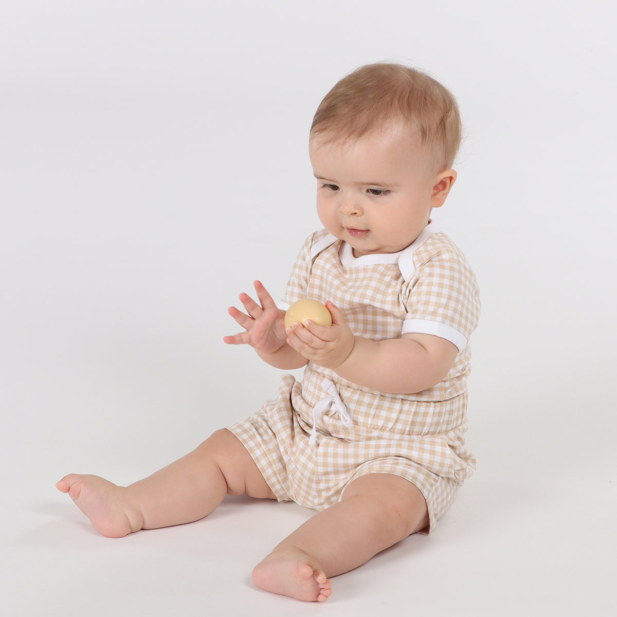 Baby playing with ball wearing organic cotton shorts and bodysuit in gingham pattern and draw string