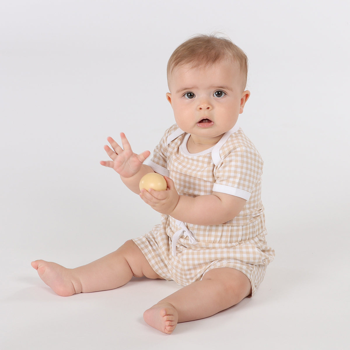 Baby playing with ball wearing organic cotton shorts and bodysuit in gingham pattern and draw string