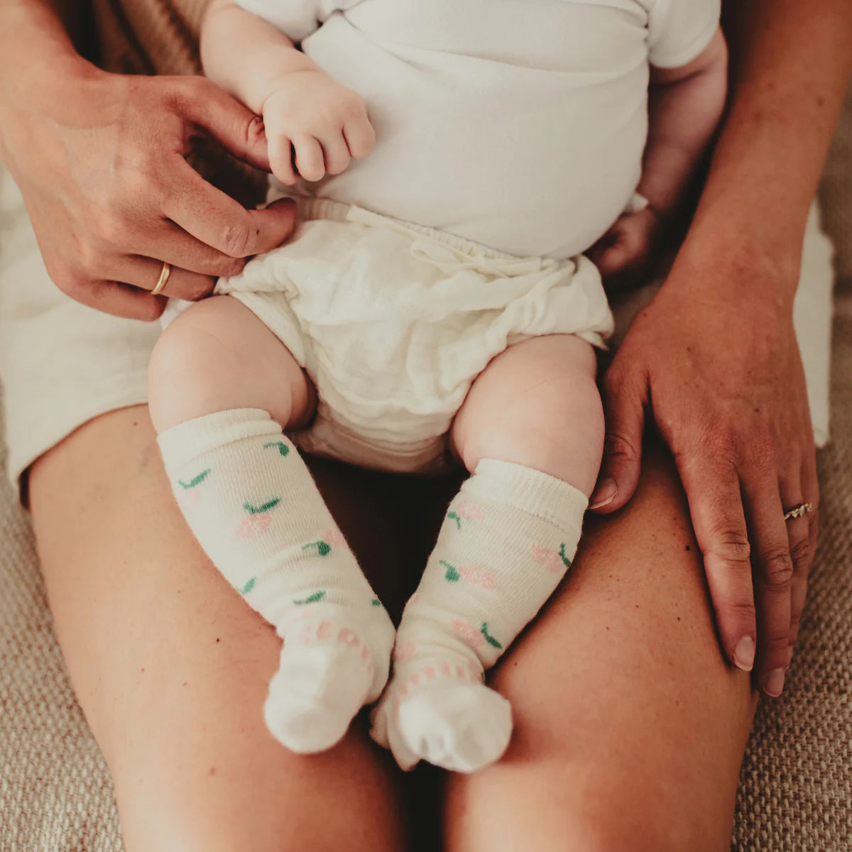 Baby wearing Merino Wool Kneehigh Socks for baby from Lamington with printed rose sitting on mothers lap