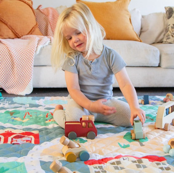 Baby girl playing on quilted playmat in tiny town print from Zazi