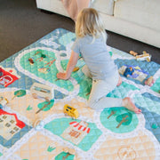 Baby girl playing on quilted playmat in tiny town print from Zazi