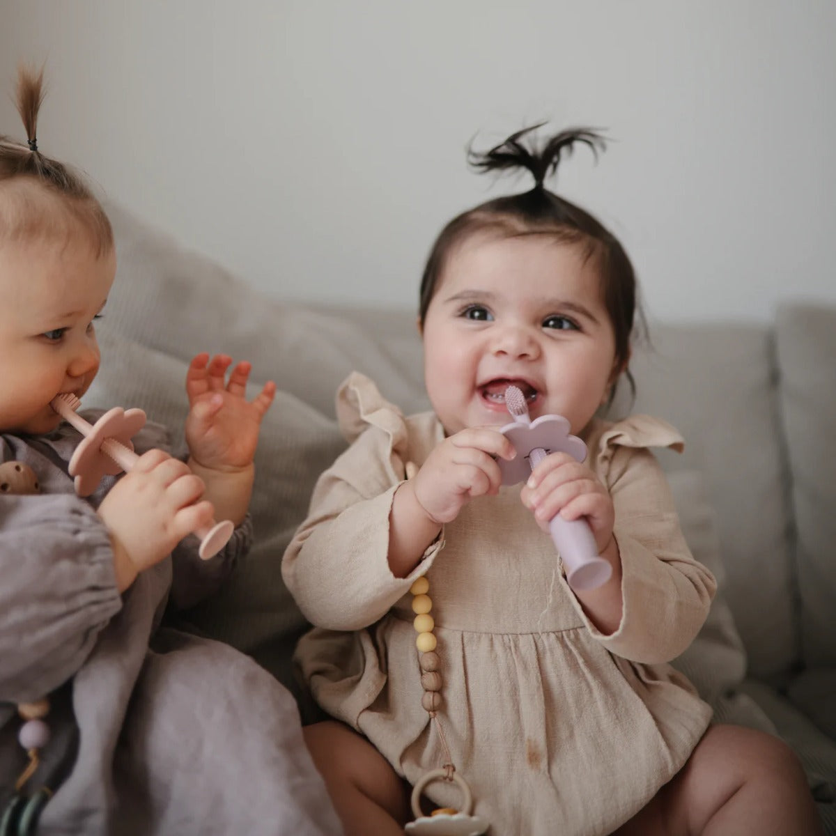 happy baby girls playing with flower training toothbrush for baby from Mushie.