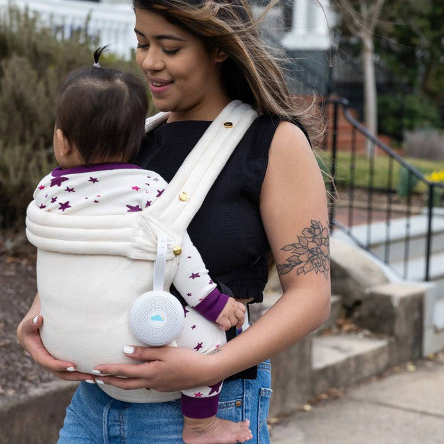 Mother carrying baby in a baby carrier outdoor with Yogasleep Hushh+ attached with the baby carrier