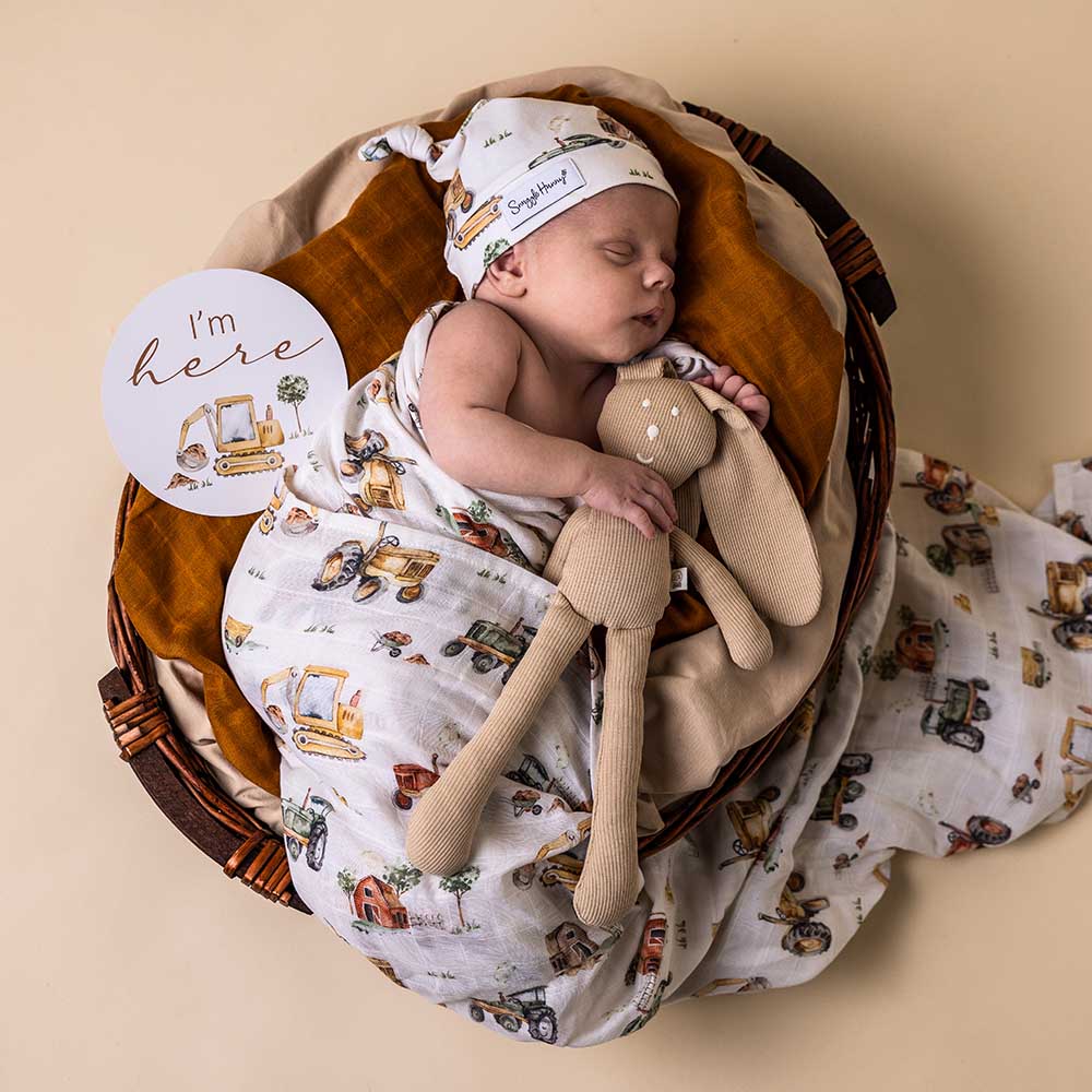 Baby sleeping in a basket wrapped in Organic Cotton Muslin Wrap in Diggers and Tractors print from Snuggle Hunny with a bunny