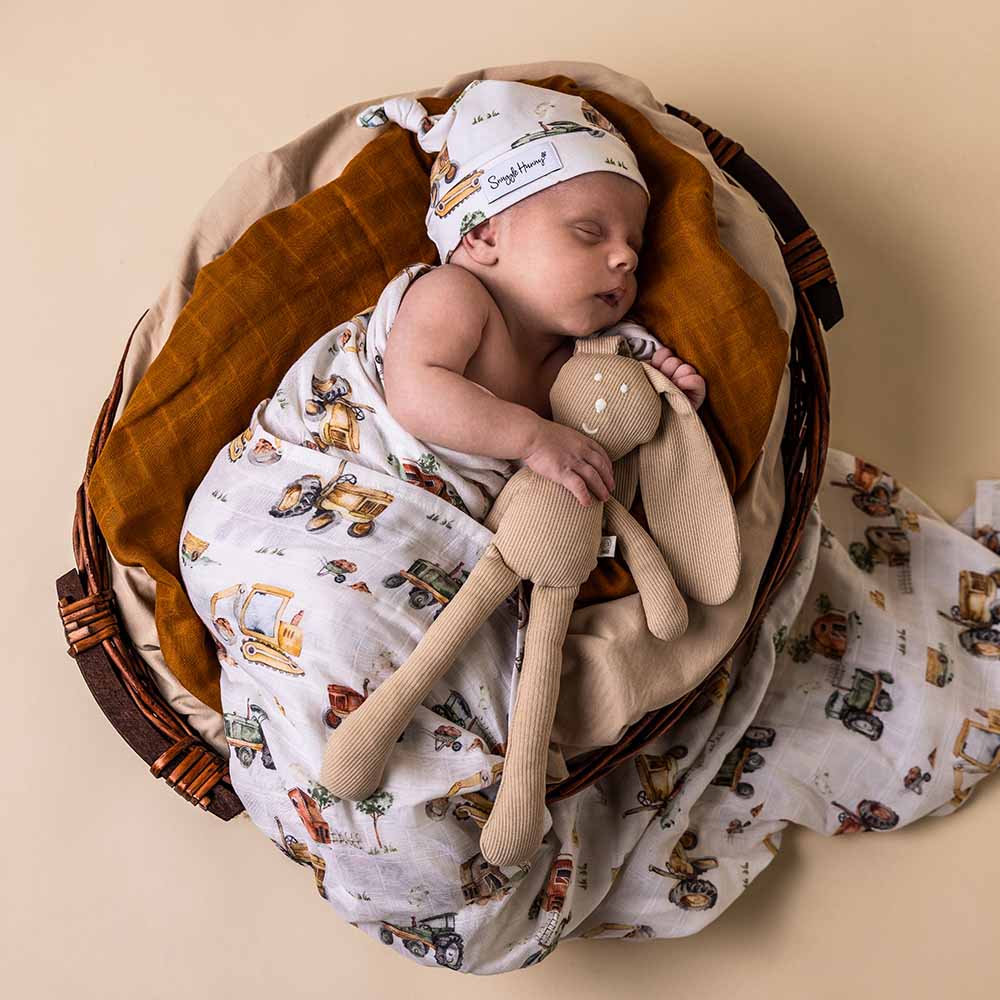 Baby sleeping in a basket wrapped in Organic Cotton Muslin Wrap in Diggers and Tractors print from Snuggle Hunny with a bunny