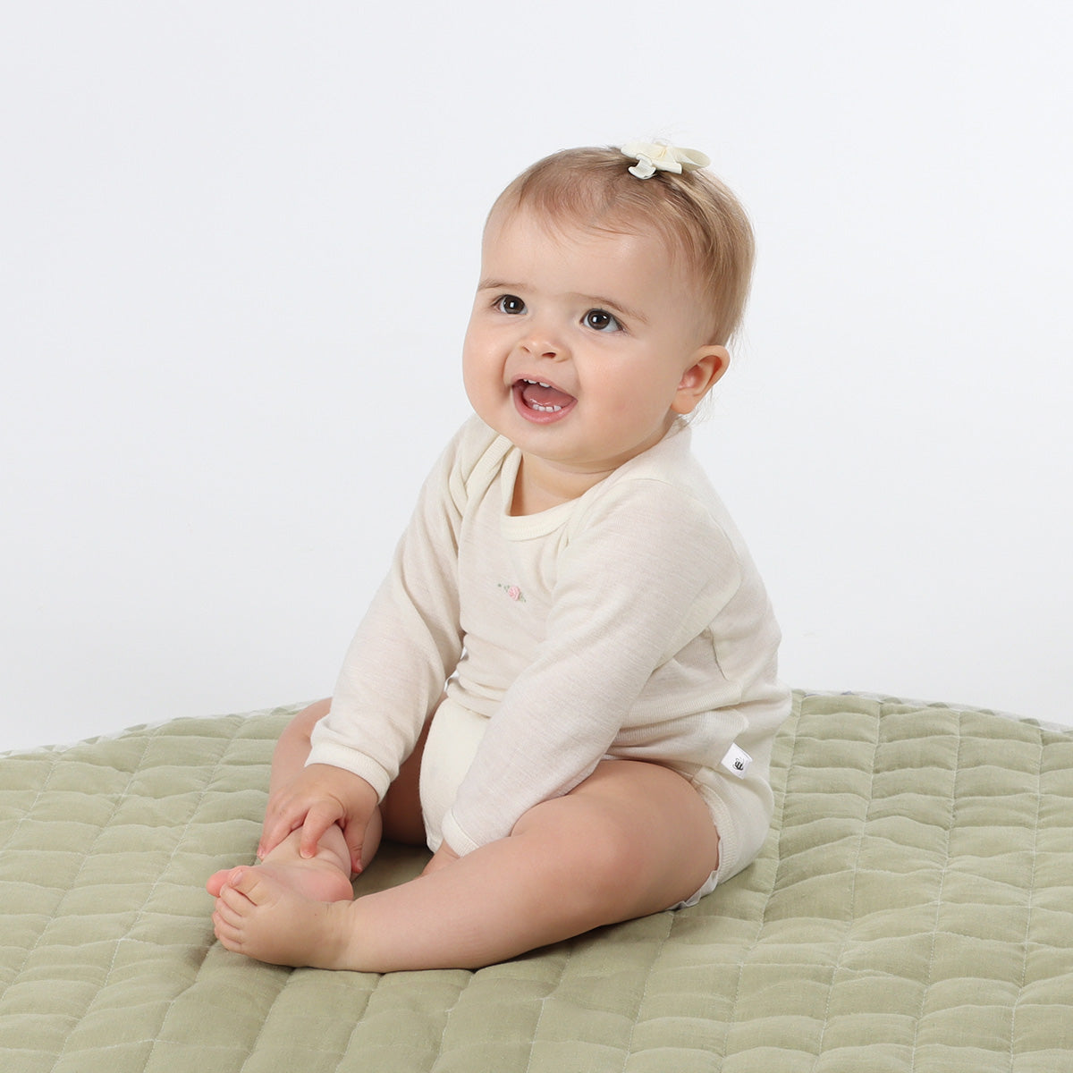 Baby girl wearing merino bodysuit sitting on a playmat