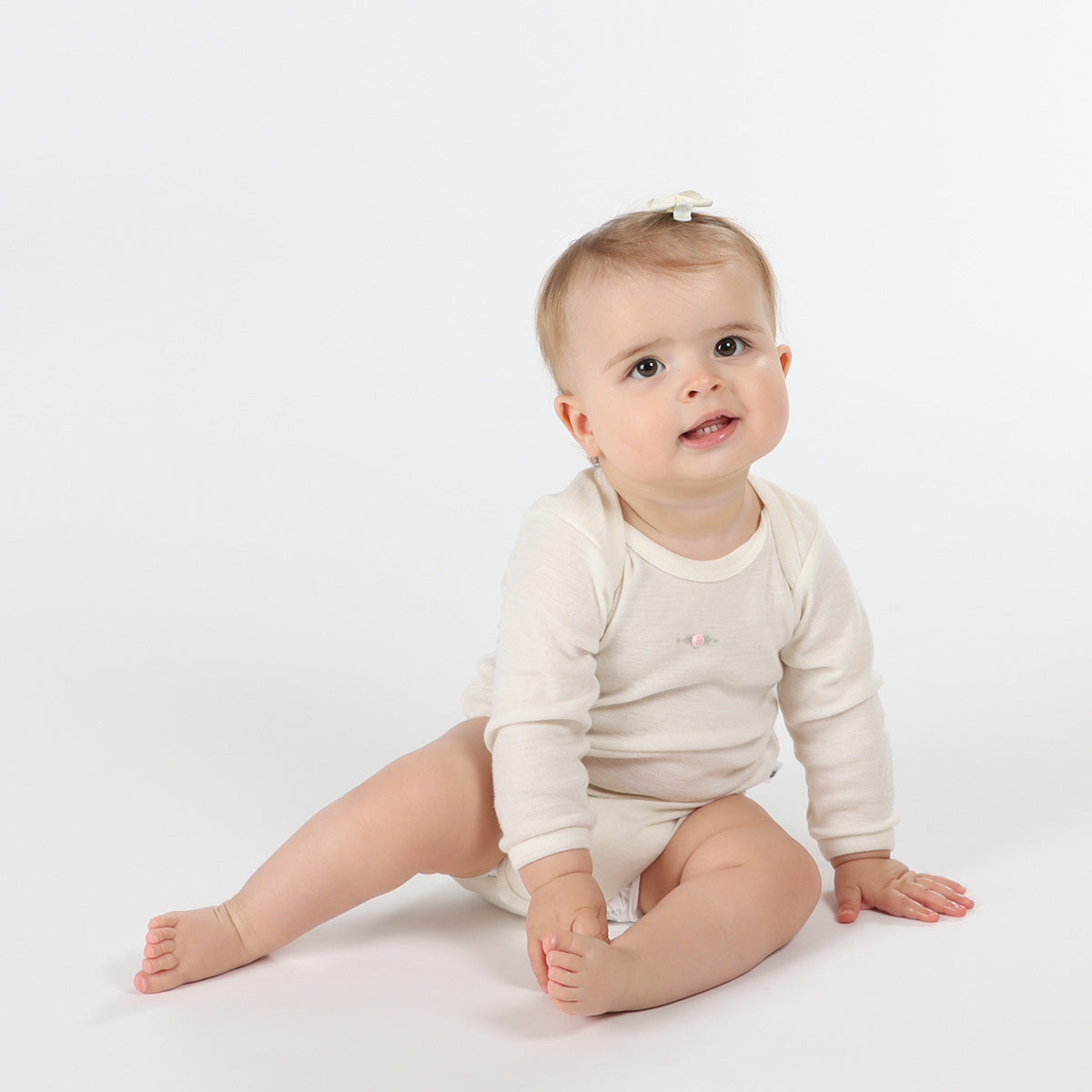 Baby girl wearing merino bodysuit sitting on a floor