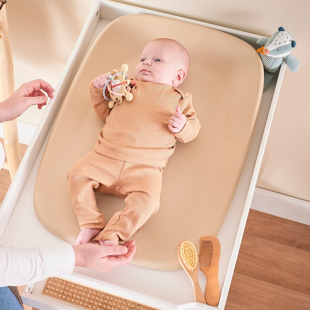 Baby playing with toy lying on Baby Change Mat from Nattou in beige