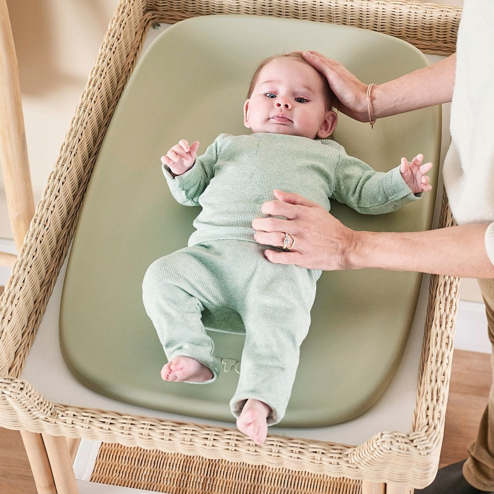 Baby lying on a Baby Change Mat from Nattou in green in a change bathroom basket