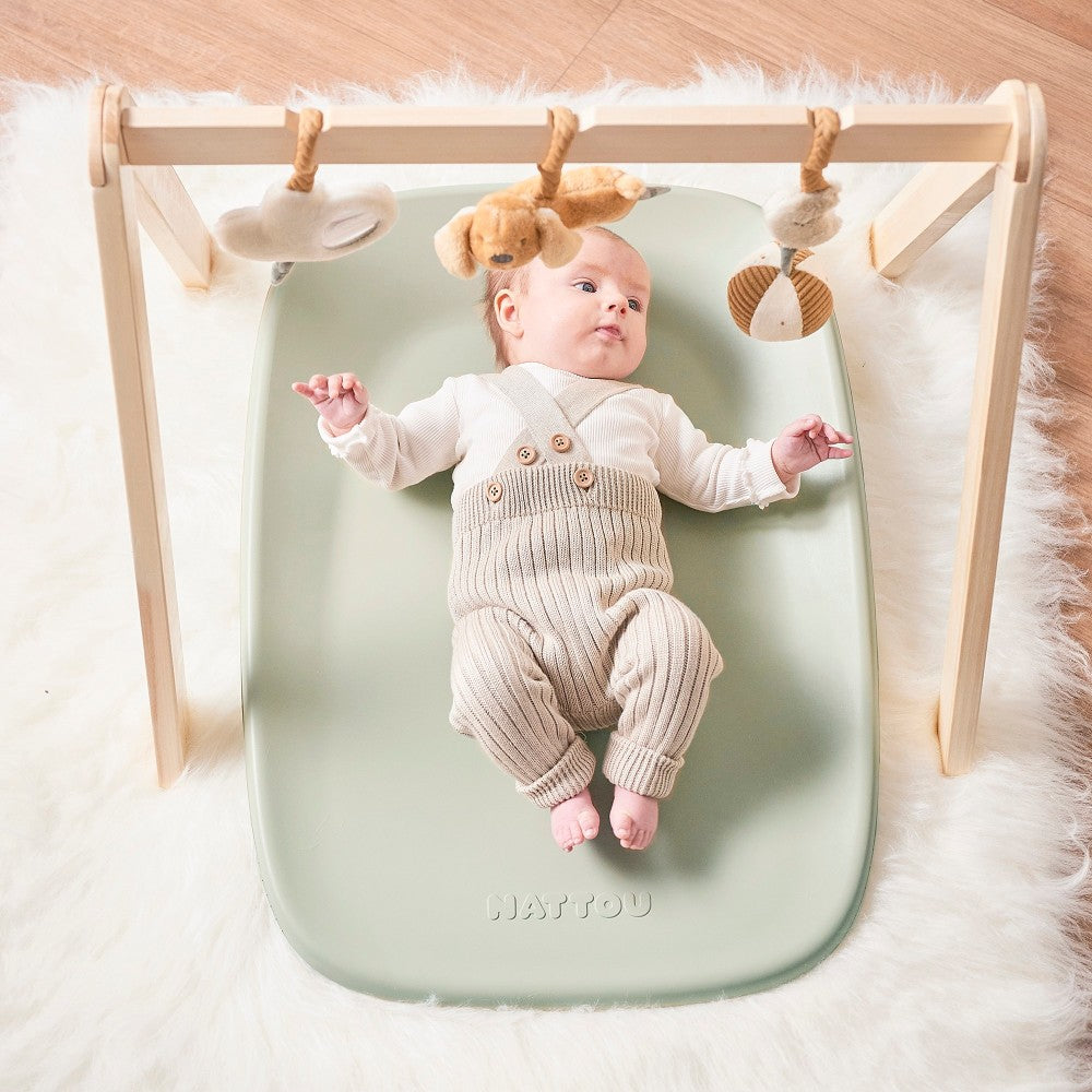 Baby playing on Baby Change Mat from Nattou in green with toy bar