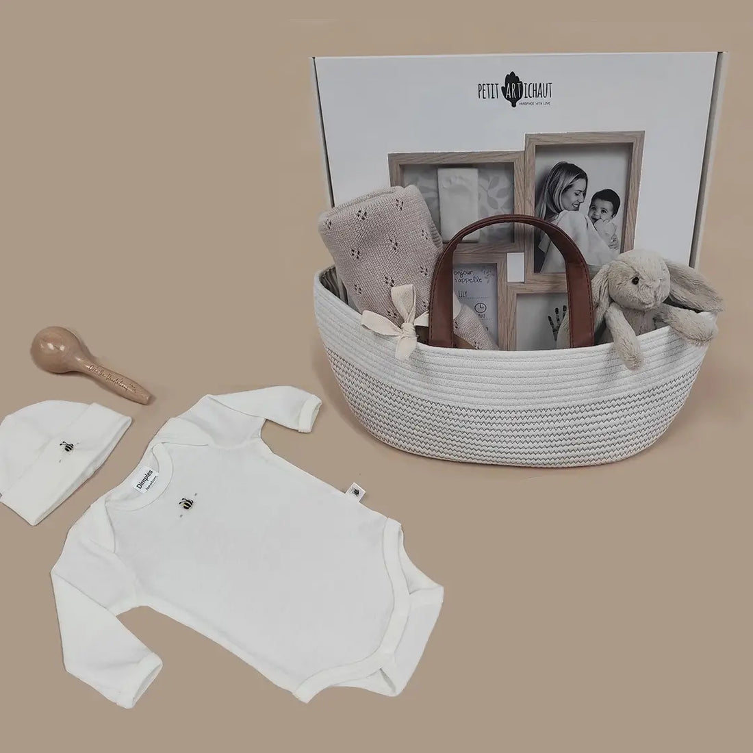 Baby gift set with white onesie, wooden spoon, and basket on a beige background