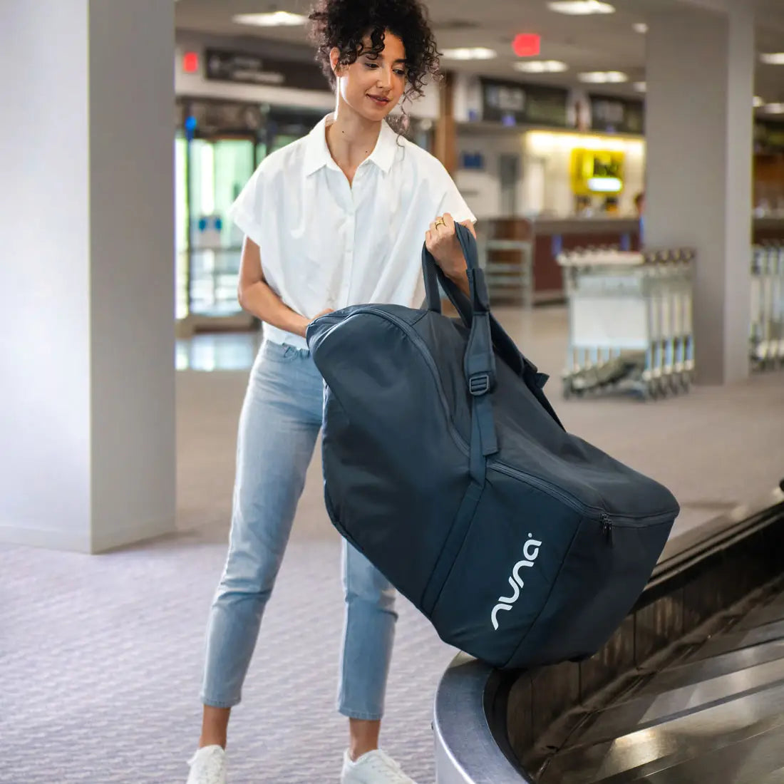 Lady taking Nuna Pipa Travel Bag in indigo from airport luggage bag