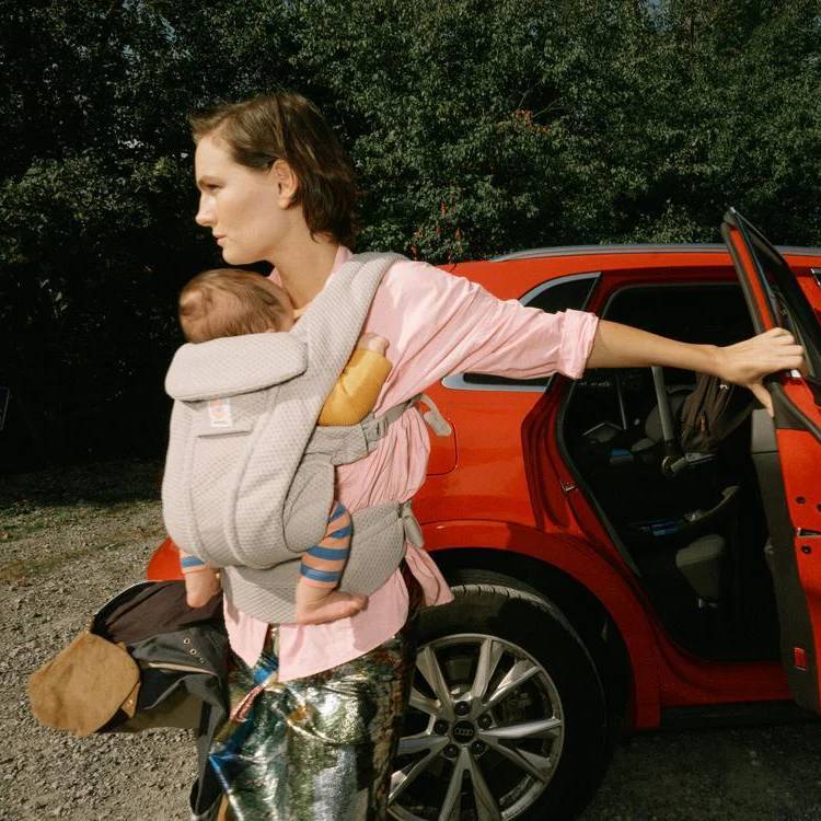 Mother carrying baby in grey mesh baby carrier in car park