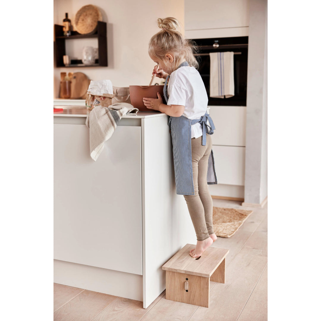 Girl in a kitchen wearing Oyoy denim apron playing with utensils.