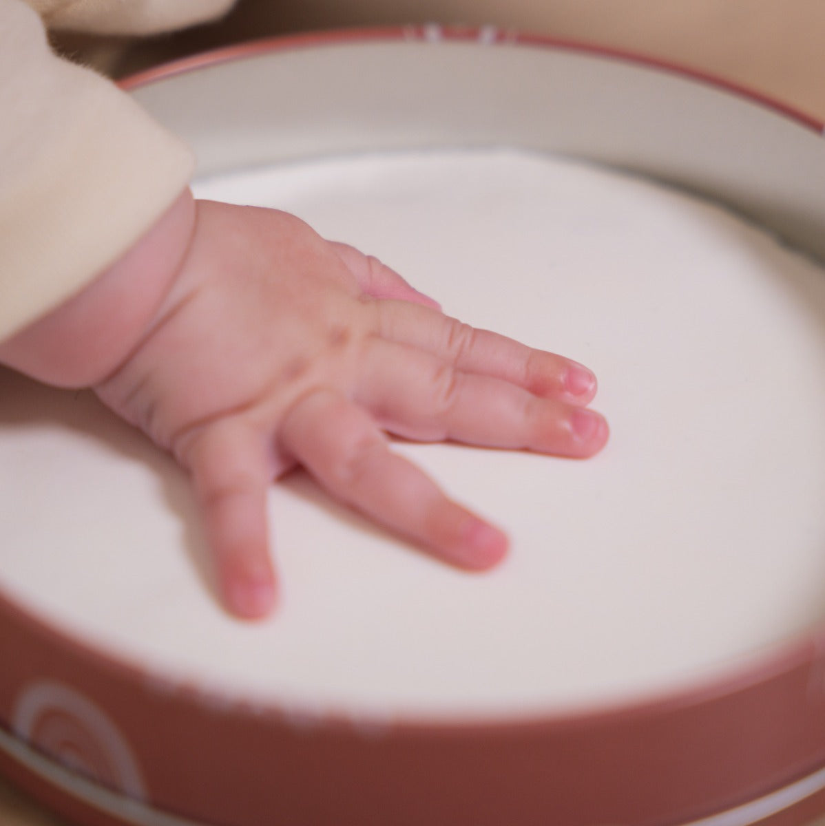 Baby hand in Petite artichaut baby box round in rainbow terracotta creating a print