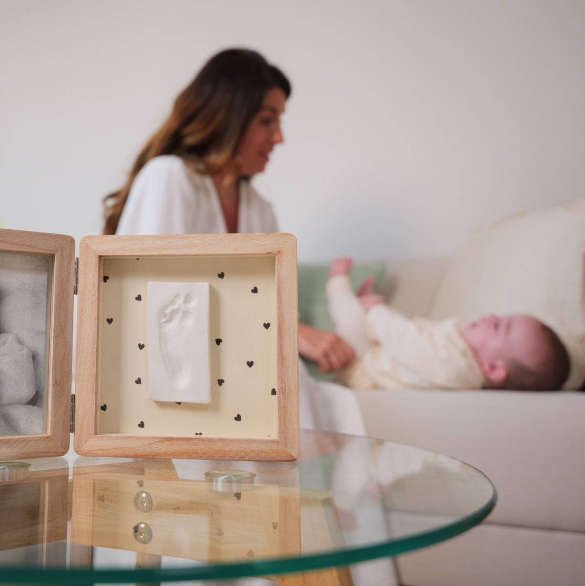 Mother tending to baby with Petit Artichaut Double Frame Pretty hearts print placed on side table 
