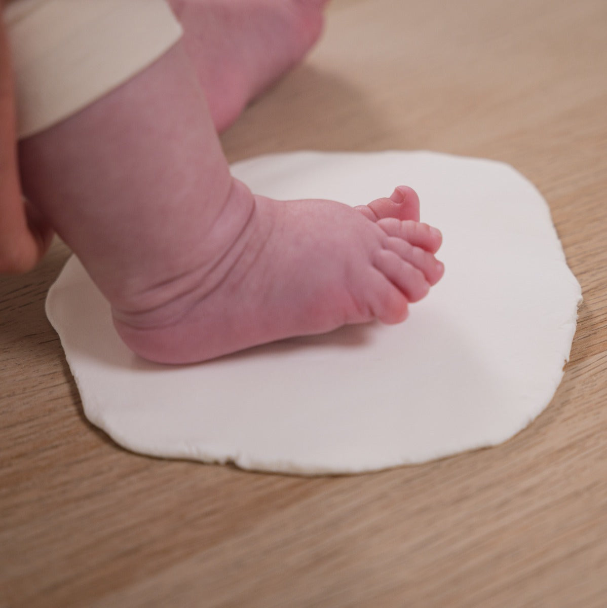 Parents taking baby footprint on modelling clay in Petit Artichaut puzzle frame baby keepsake