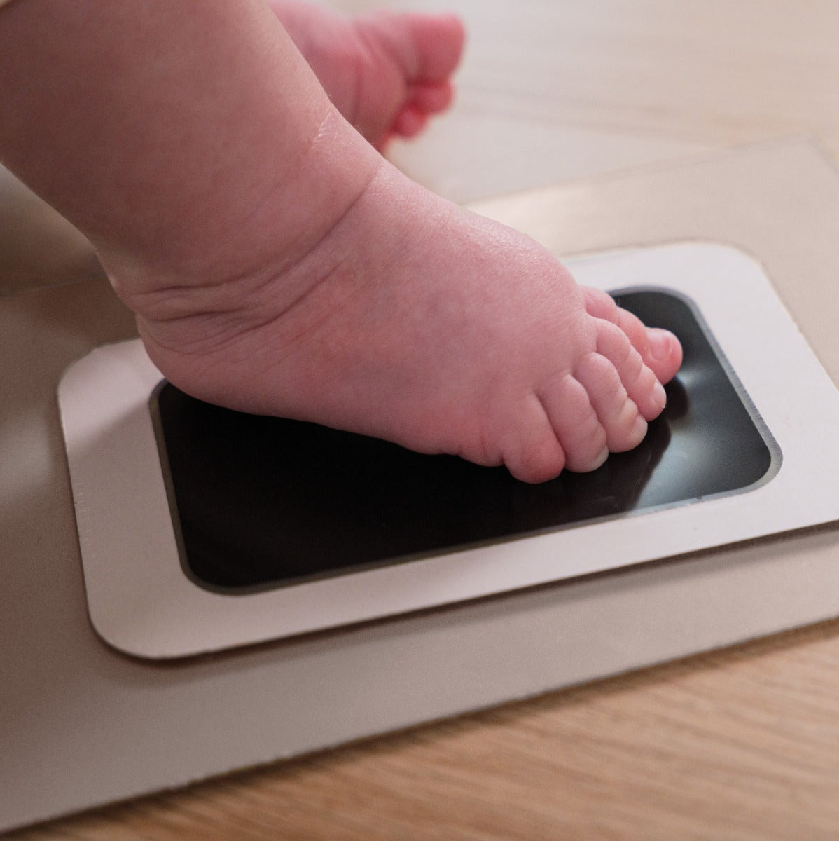 Parents taking imprint of a baby feet on a Petit Artichaut 4 wooden memory frames