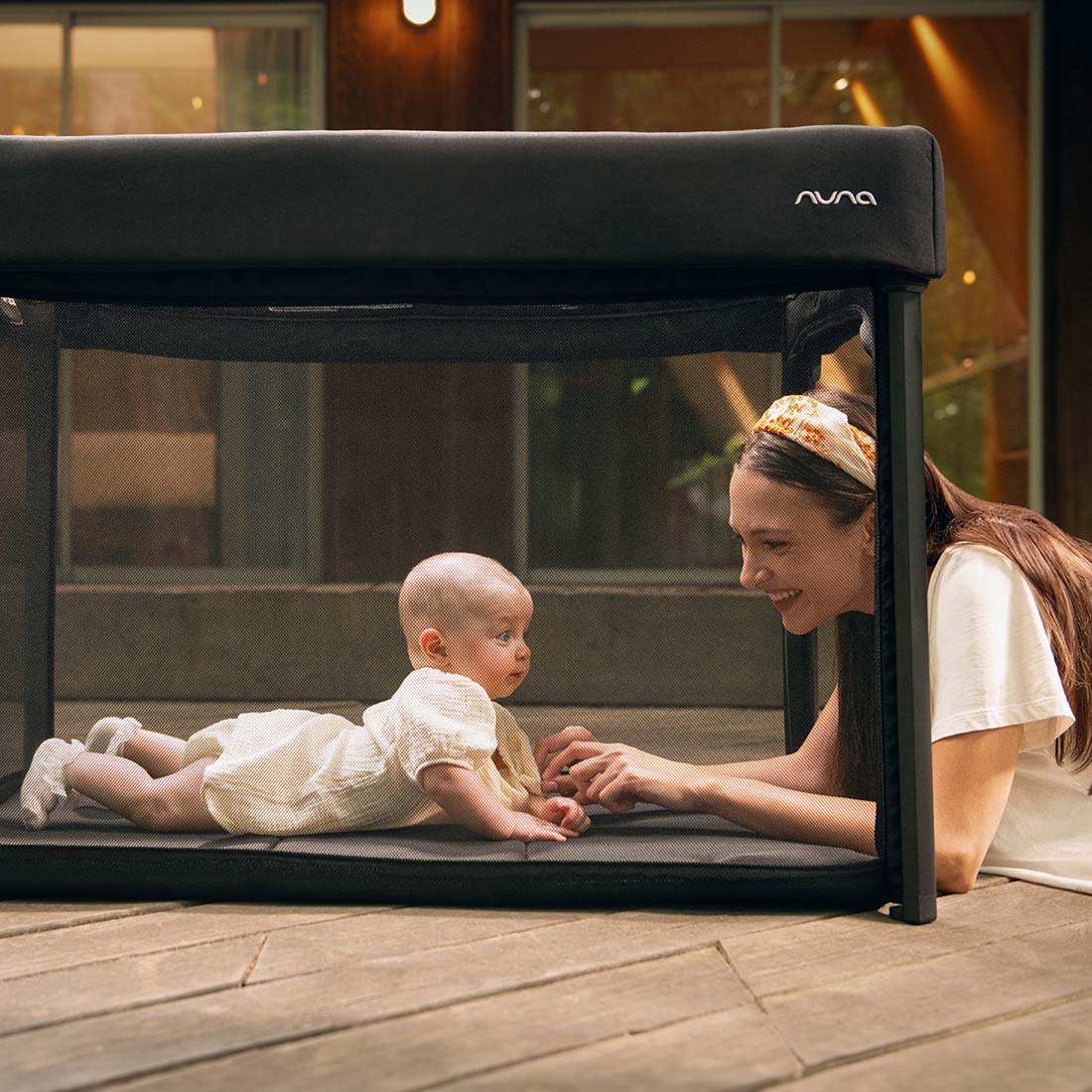 Baby and mother playing in Nuna Paal bassinet and travel cot in caviar