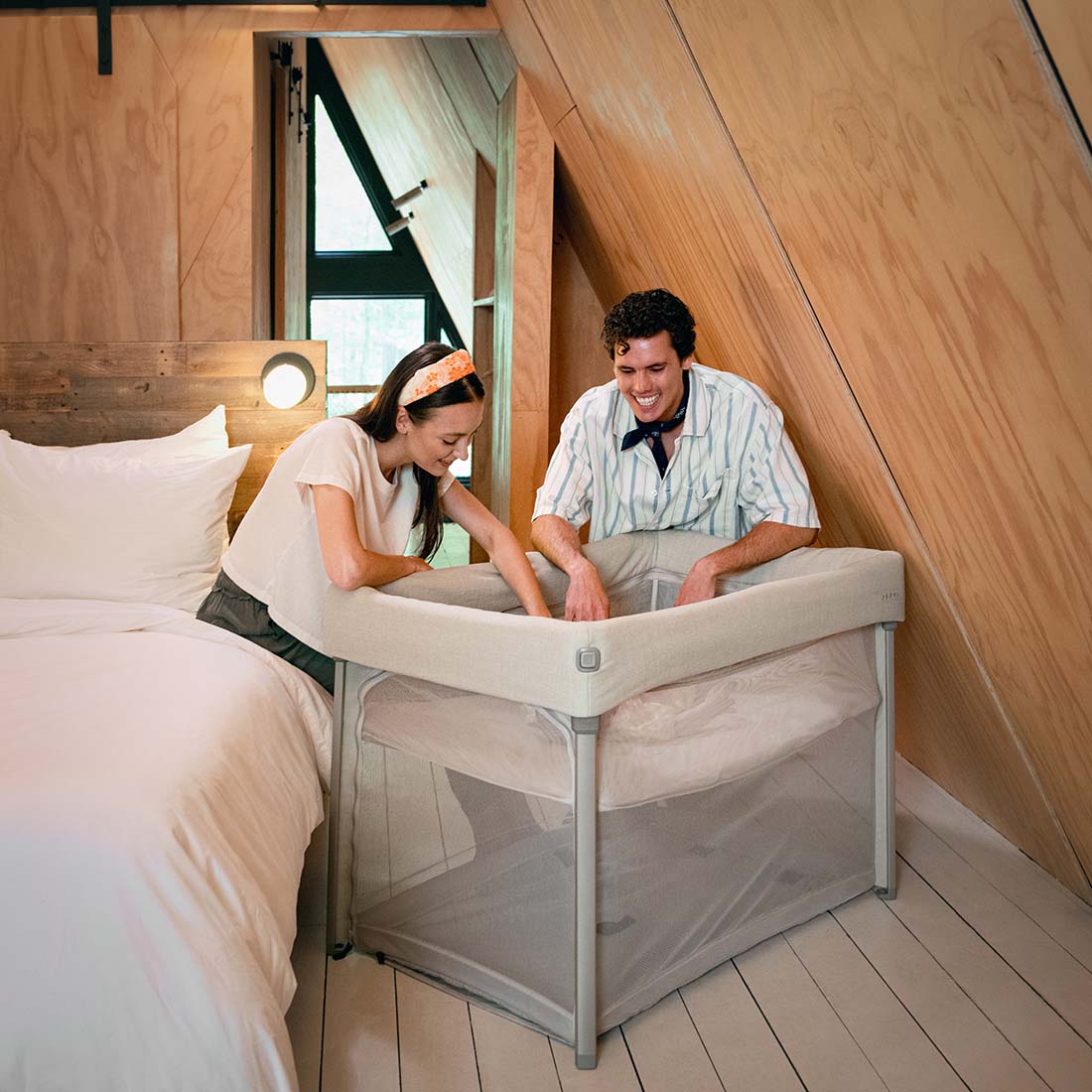 Parents putting baby to sleep in Nuna Paal bassinet and travel cot in caviar in  holiday home