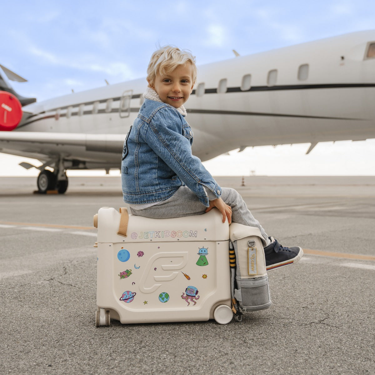 Happy kid sitting on a stokke jetkids bedbox in white with stickers near airplane