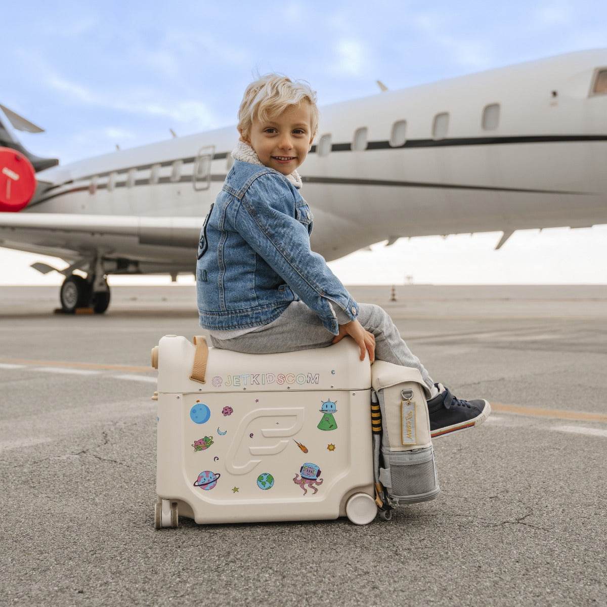 Happy kid sitting on a stokke jetkids bedbox in white with stickers near airplane