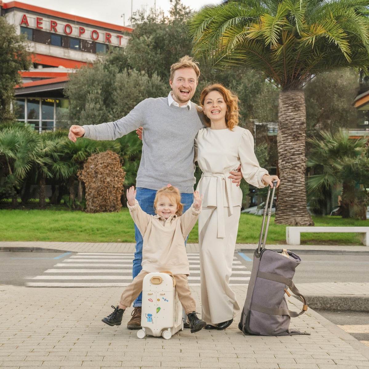 Happy family travelling with kid sitting on a white stokke jetkid bedbox outside airport