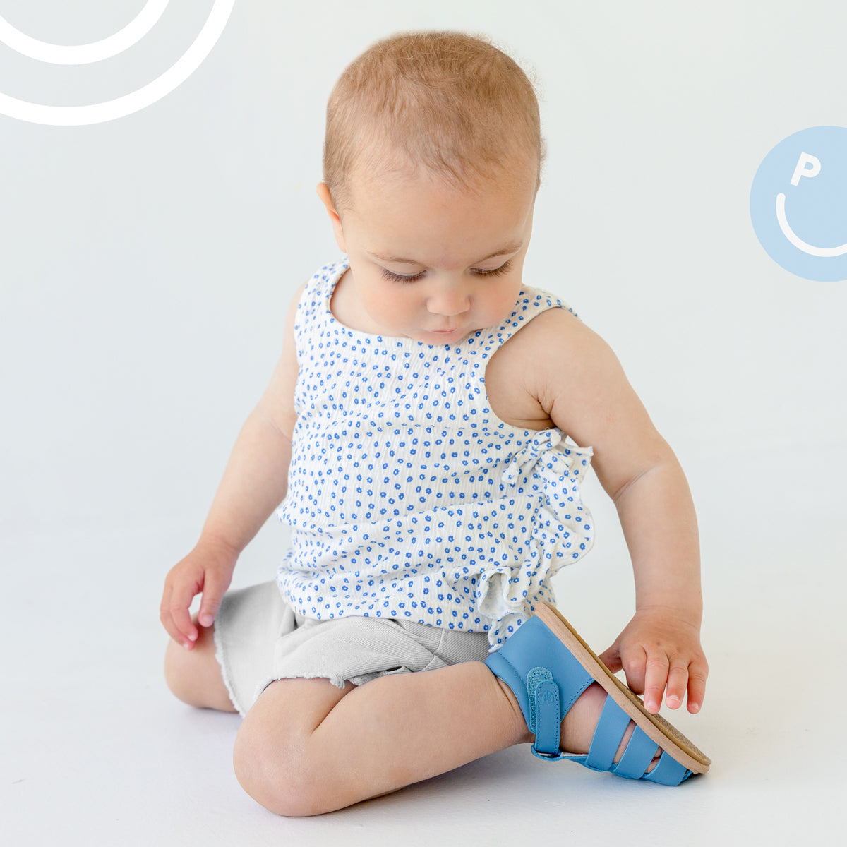 Baby sitting down wearing Pretty Brave Rio Baby Sandals in Playground Blue side