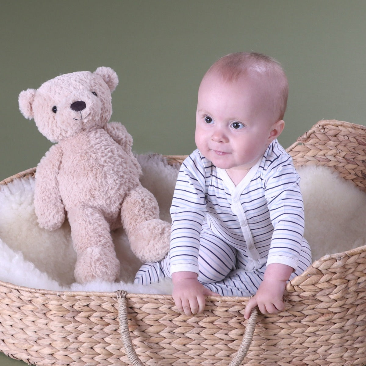 Baby boy wearing Cotton Stripe Babygrow with button sitting in a basket with bear plush toy