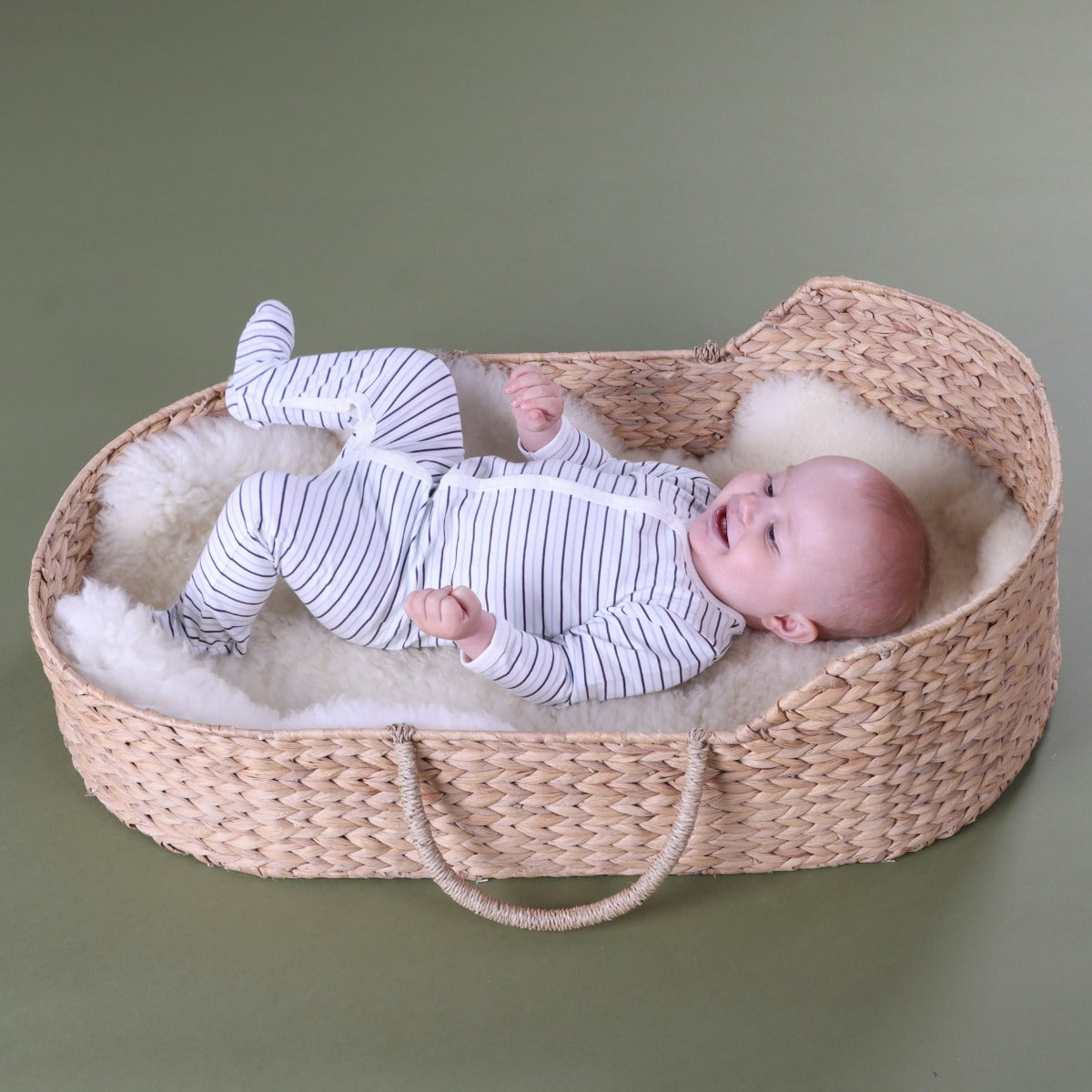 Baby boy wearing Cotton Stripe Babygrow with button sleeping in a basket