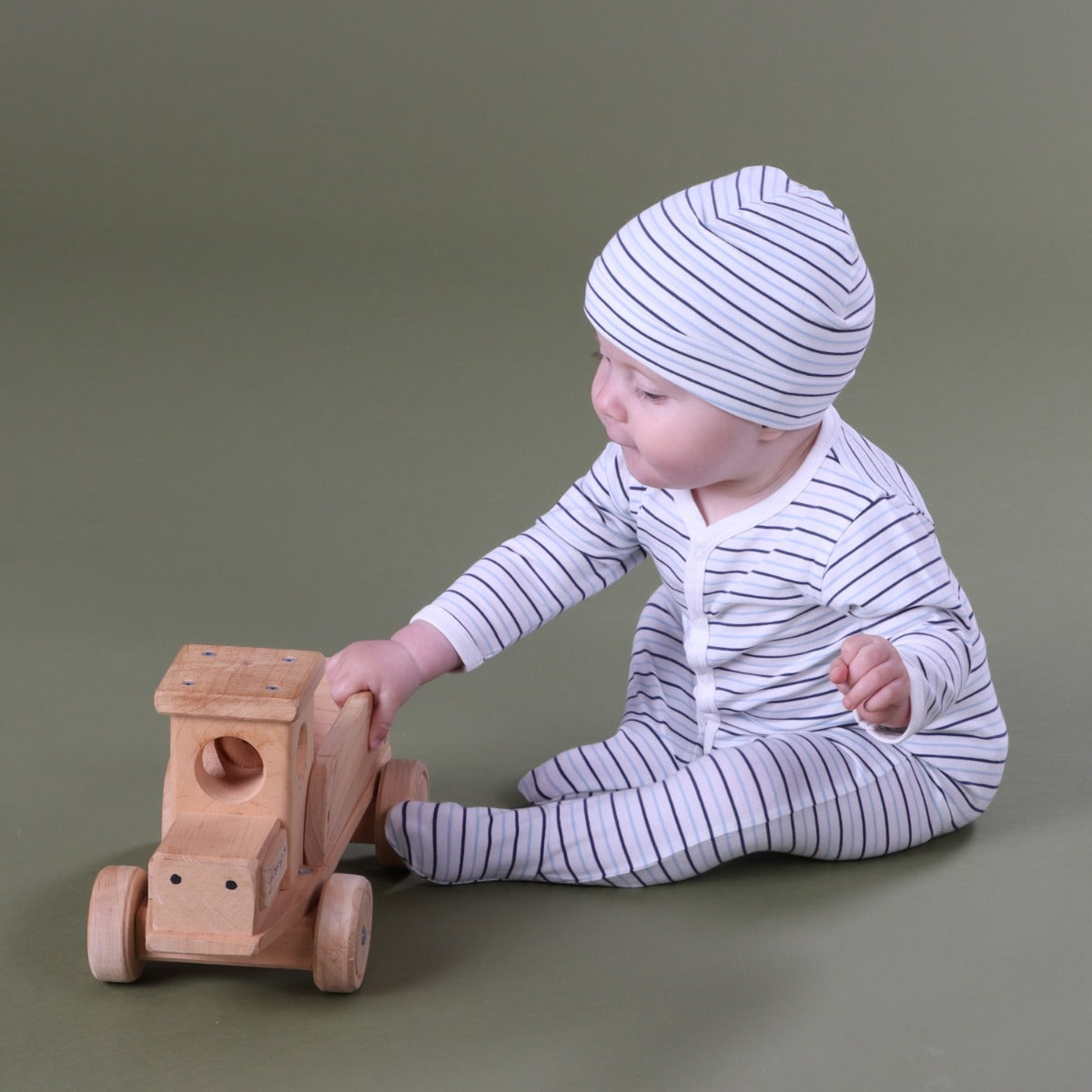 Baby boy wearing Cotton Stripe Babygrow with button with beanie and playing with toy truck.