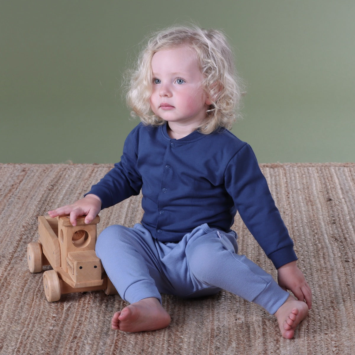 Baby boy sitting with a toy truck wearing navy cotton jacket pairing it with merino pant