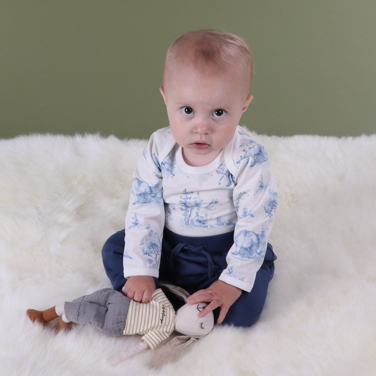 Baby boy sitting on a rug wearing wolf and bear print long sleeve body suit paired with navy cotton pant