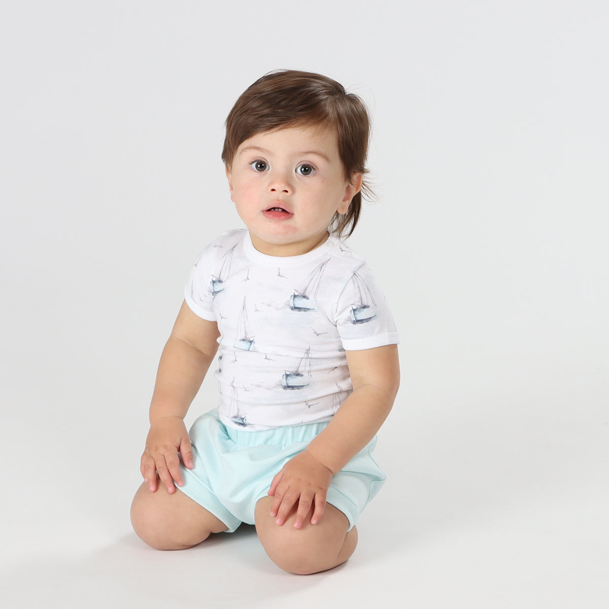 Baby wearing organic cotton bodysuit with boats print pairing it with blue shorts