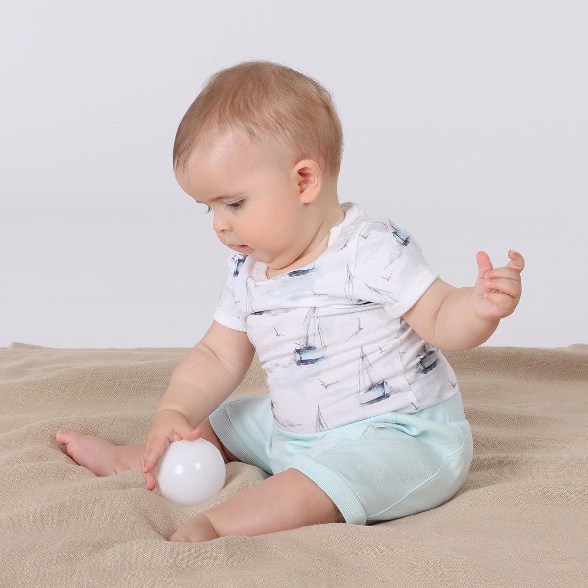 Baby wearing organic cotton bodysuit with boats print pairing it with blue shorts