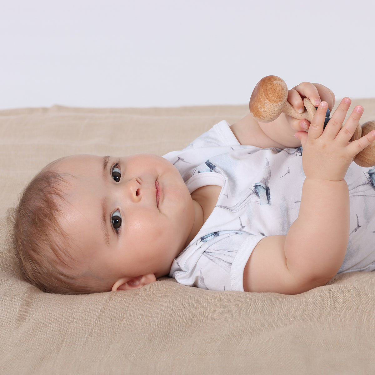 Baby playing with rattle wearing organic cotton bodysuit with boats print pairing it with blue shorts