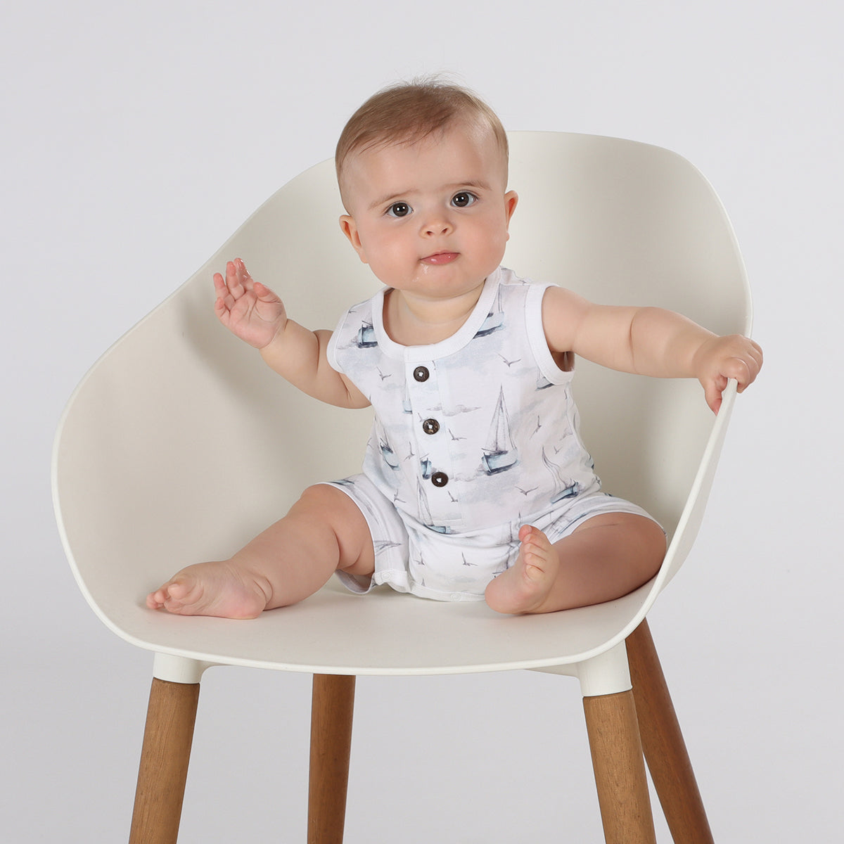 Baby sitting on chair wearing organic cotton tank romper with boats print