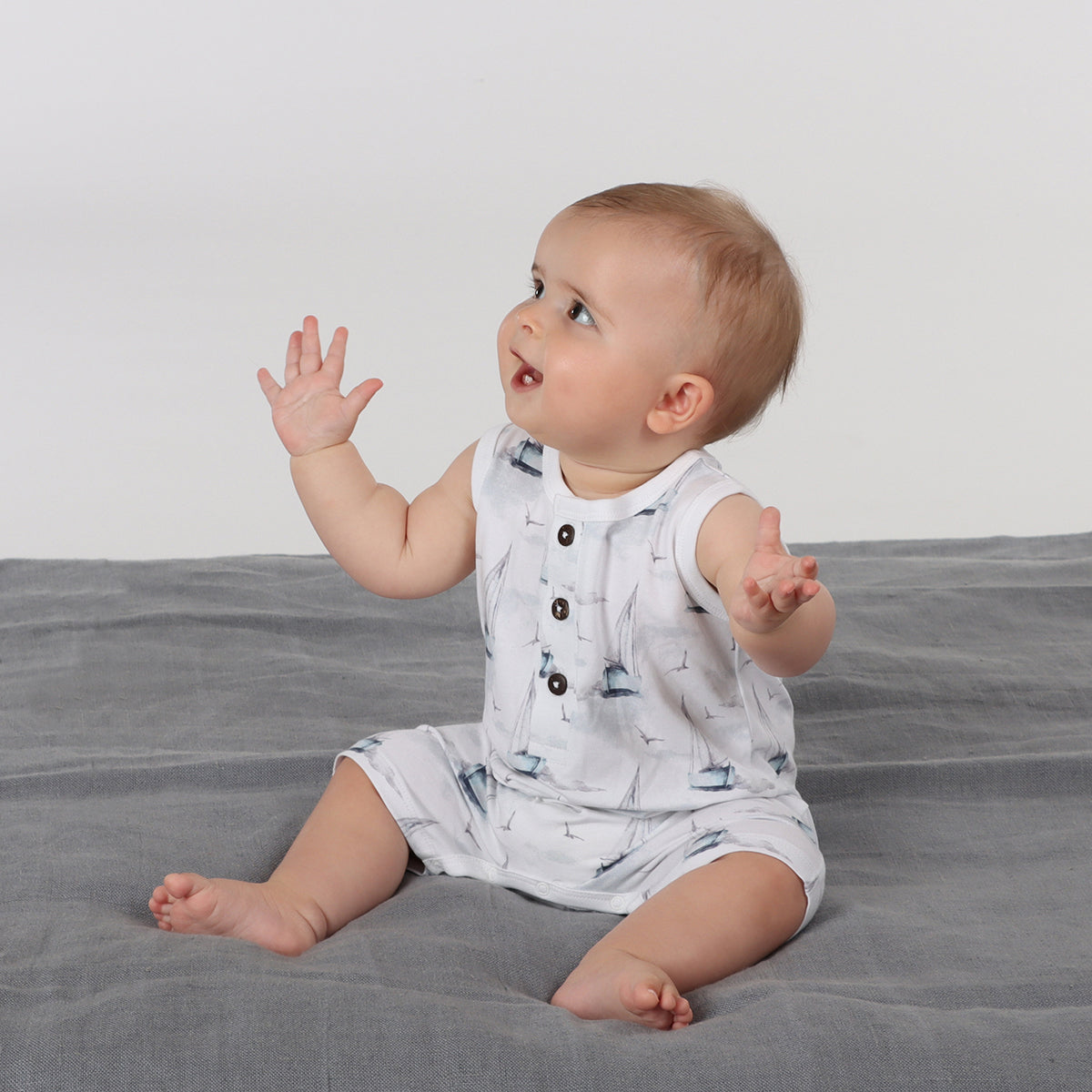 Baby sitting on rug wearing organic cotton tank romper with boats print