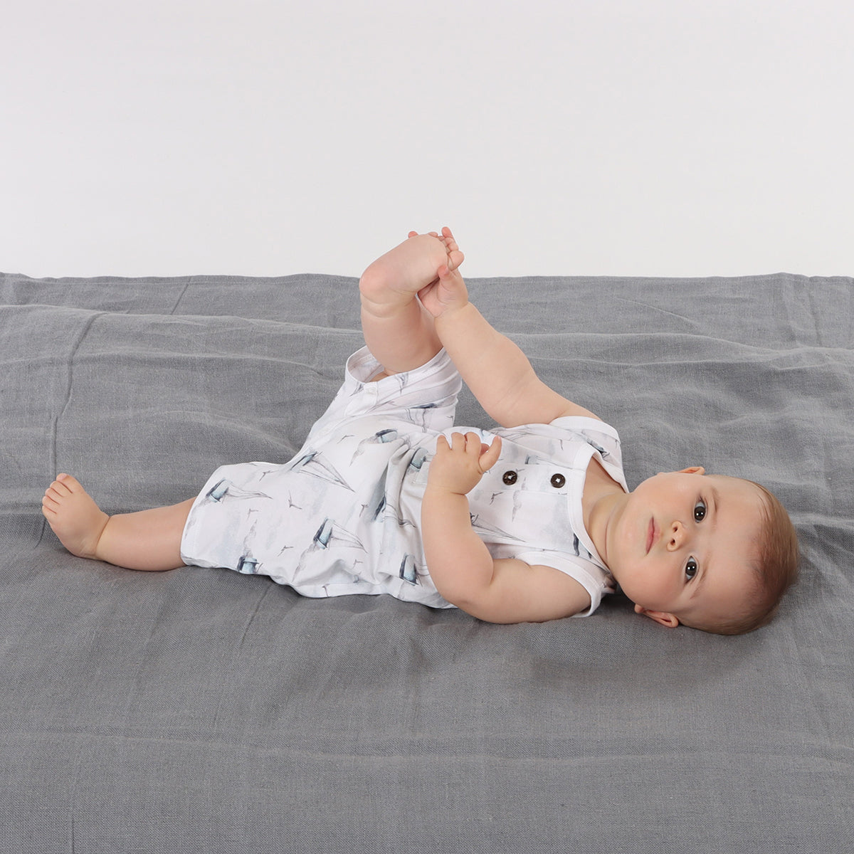 Baby sleeping on rug wearing organic cotton tank romper with boats print