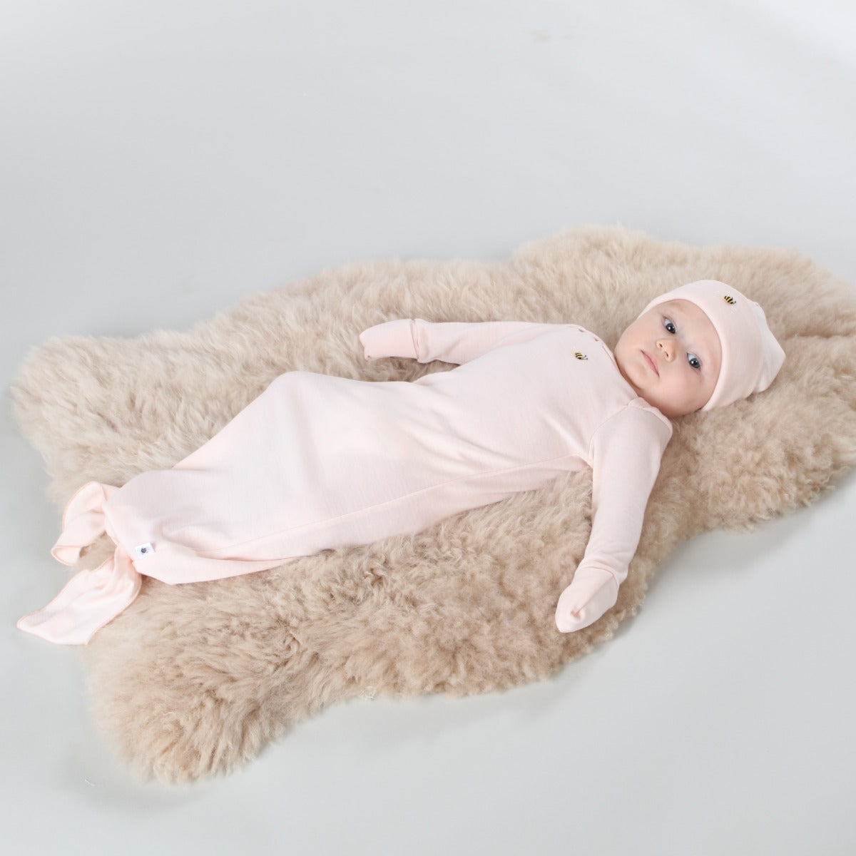 Baby girl wearing tie gown, beanie and mitten, lying down on a rug
