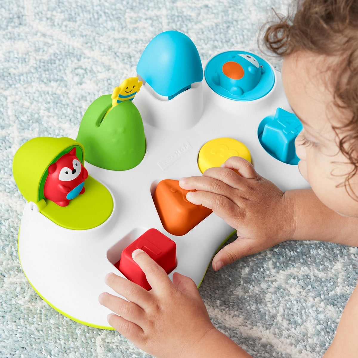 Hand pressing buttons of Explore & More Pop Up Toy from Skip Hop