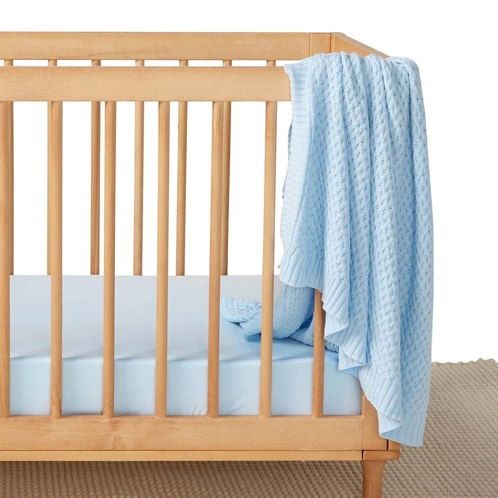 Snuggle Hunny Baby Blue Diamond Knit Baby Blanket lying on a cot railing