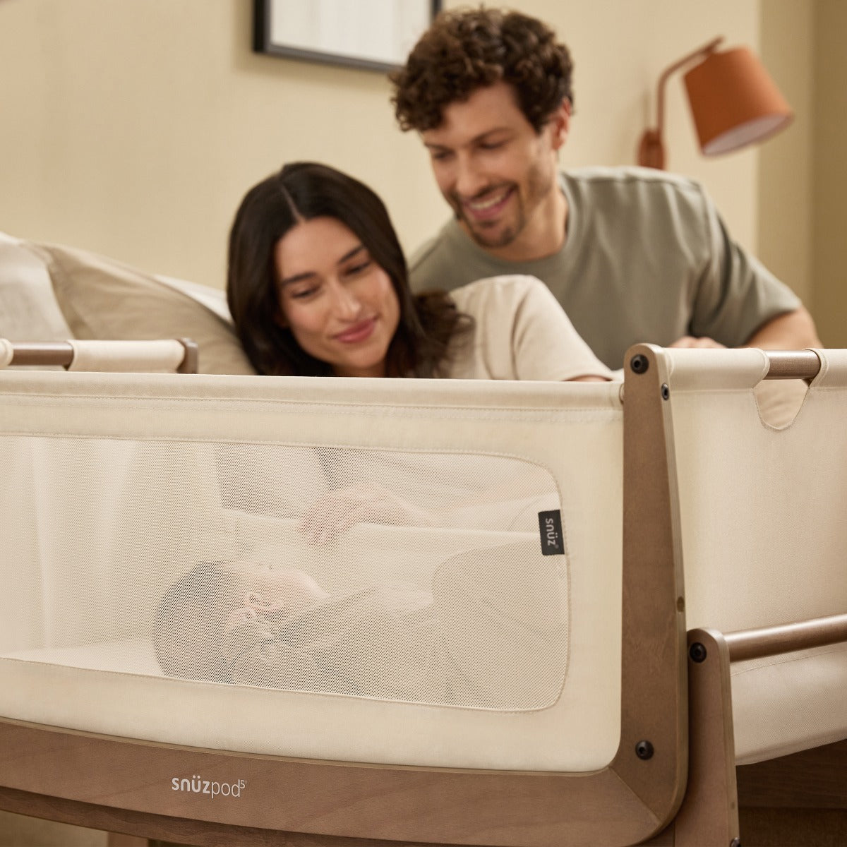Parents watching baby sleeping in Snuzpod 5 Walnut Wood Frame Bedside Baby Crib