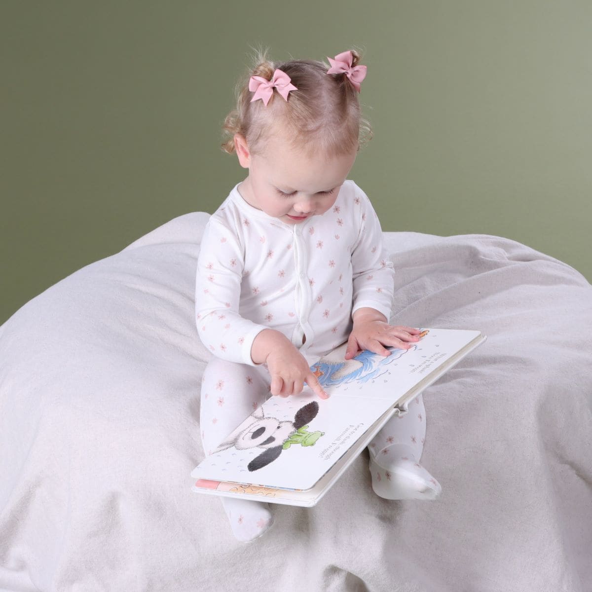 Baby girl sitting on a lounger reading book wearing dainty floral baby grow