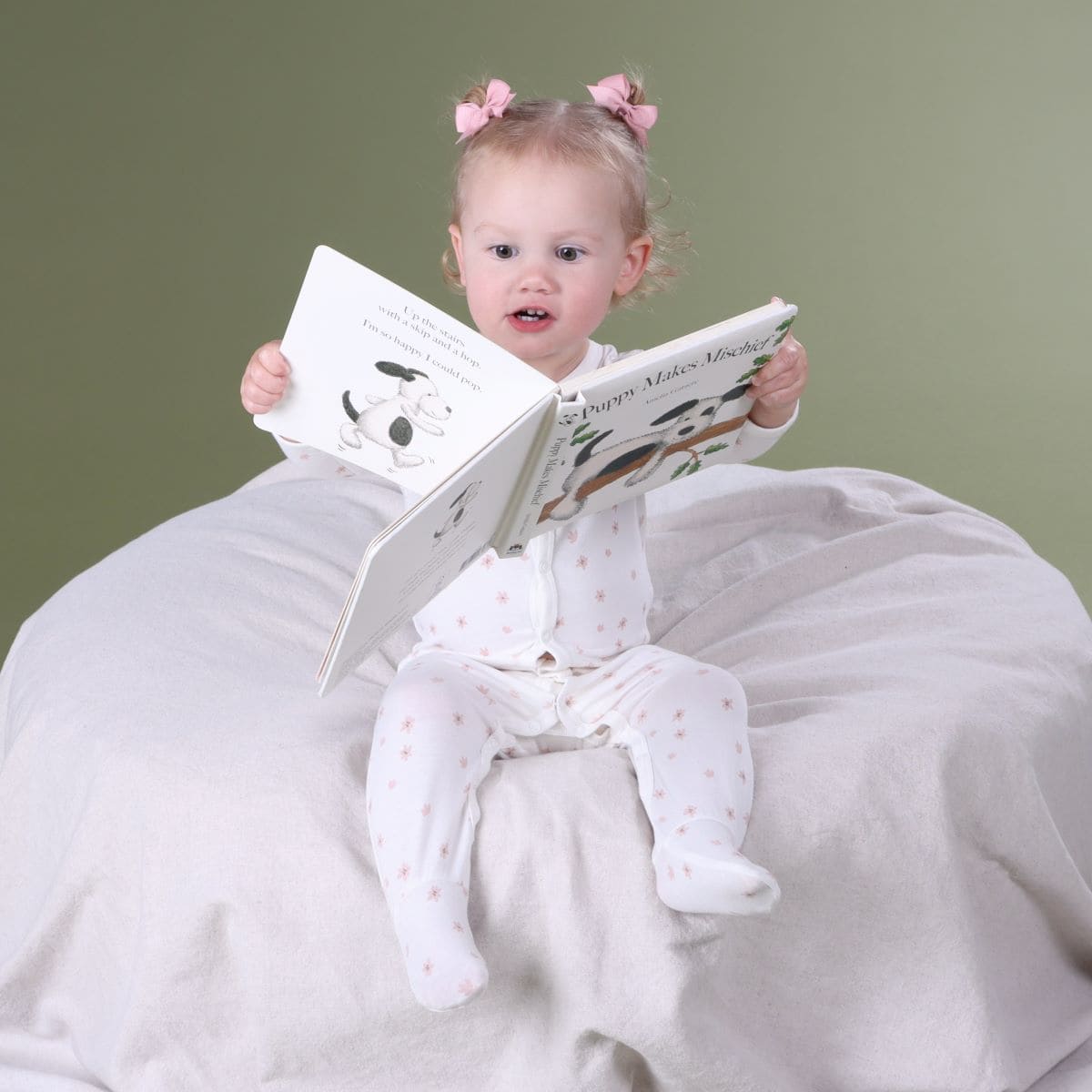 Baby girl sitting on a lounger reading book wearing dainty floral baby grow